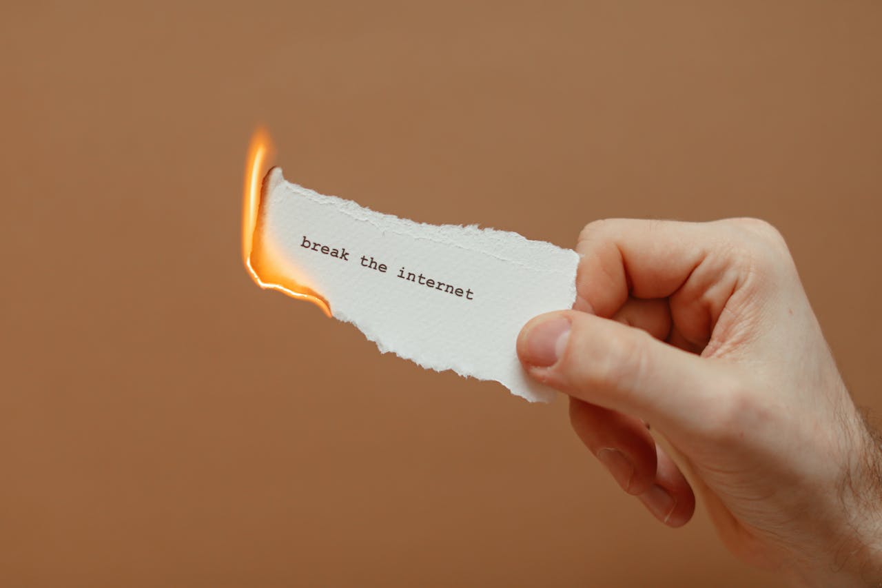Home Close-up of a hand holding a burning paper with 'break the internet' text.