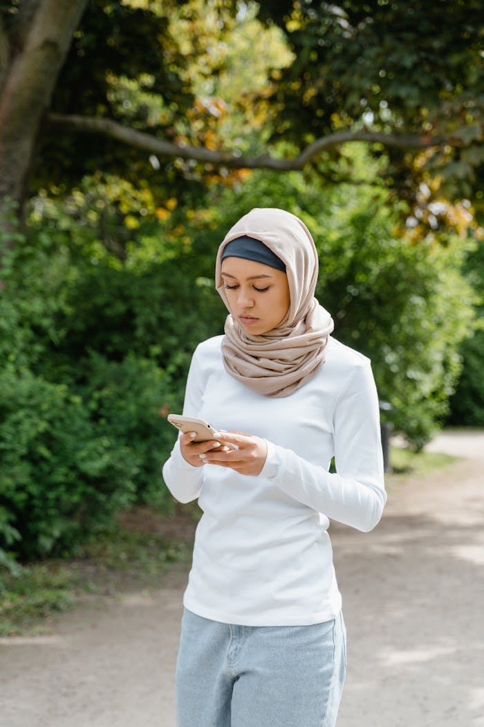 A young Muslim woman in a hijab using her smartphone while walking outdoors.